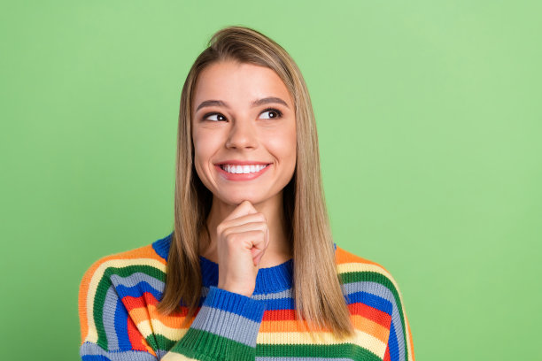 照片肖像，一位漂亮的女孩带着疑惑，若有所思地微笑，表情愉悦，孤立在柔和的绿色背景前，凝视着空白空间。图片下载