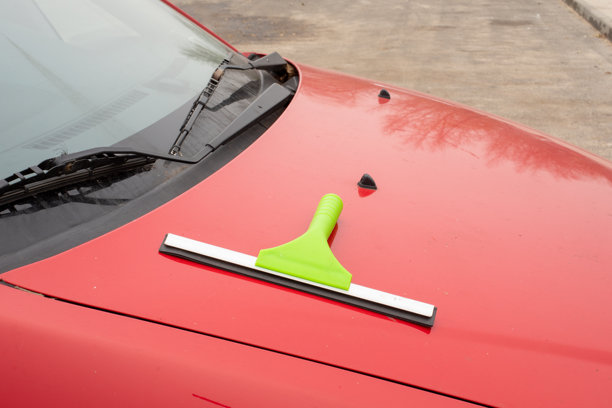 红色汽车引擎盖挡风玻璃附近有绿色刮水器。汽车清洁、汽车保养、细节处理工具。真实照片图片下载