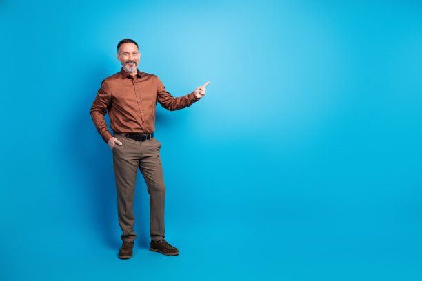 身穿棕色衬衫和西裤的男士，对着蓝色影棚背景微笑并指向前方，这是一张用于企业商务生活方式的图库照片图片下载