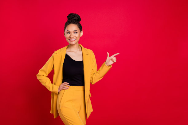 身穿黄色开衫的时尚女商人，手指着空白空间，背景为鲜艳的红色图片下载