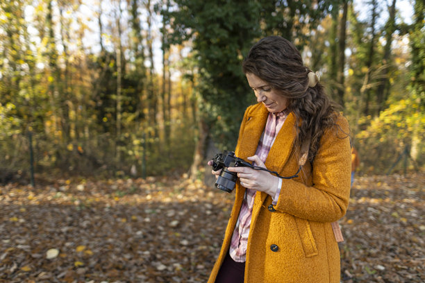 阳光明媚的秋日公园里，一位女士正在她的相机上查看照片。图片下载