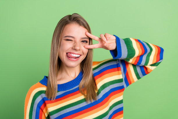 照片肖像，微笑的女孩比着V字手势，舔着嘴唇，孤立在粉绿色背景上图片下载