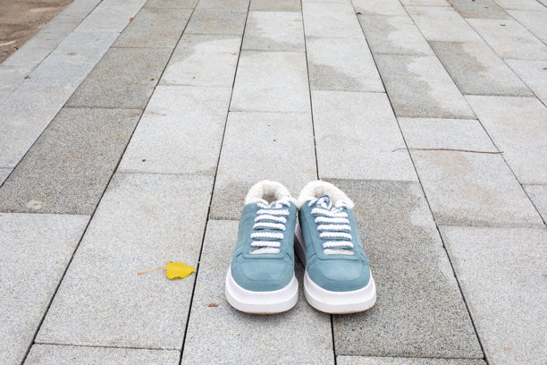 浅蓝色运动鞋放在湿漉漉的铺装地面上，旁边有一片孤零零的黄叶。鞋子、户外生活方式、季节性细节。留白。真实照片。图片下载