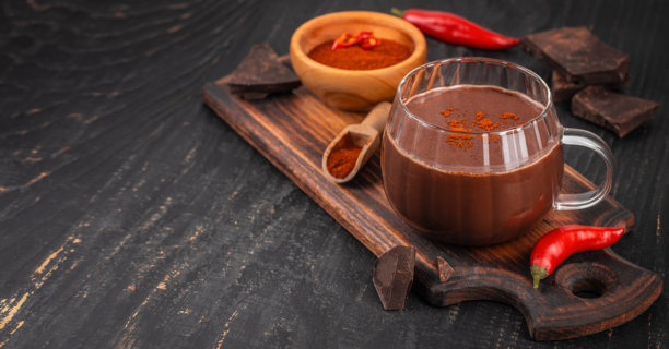 木板上的辣热巧克力，配有辣椒和可可粉，周围散落着黑巧克力块，俯视拍摄。留有复制空间。图片下载