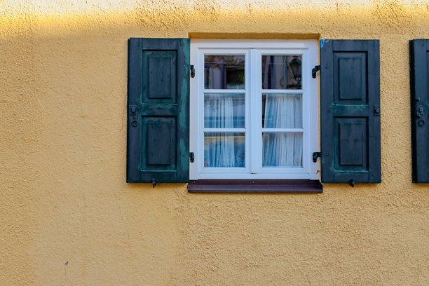 纹理黄色墙壁上迷人的复古窗户，配有绿色木制百叶窗，捕捉了温馨的建筑细节和质朴的欧洲风情。图片下载