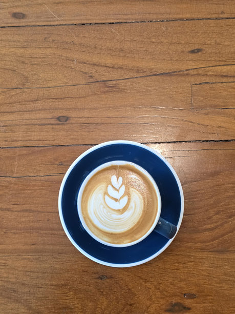 蓝色的杯子放在木桌上，里面盛着拉花精美的拿铁咖啡，散发着温馨舒适的邀请。图片下载