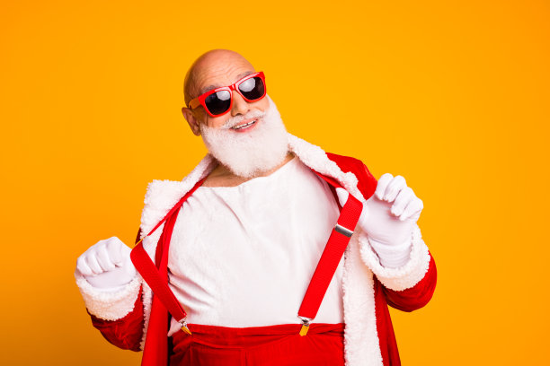 穿着红色套装、饰有白色毛皮的圣诞老人，在圣诞季戴着太阳镜，喜悦地摆姿势拍摄节日照片图片下载