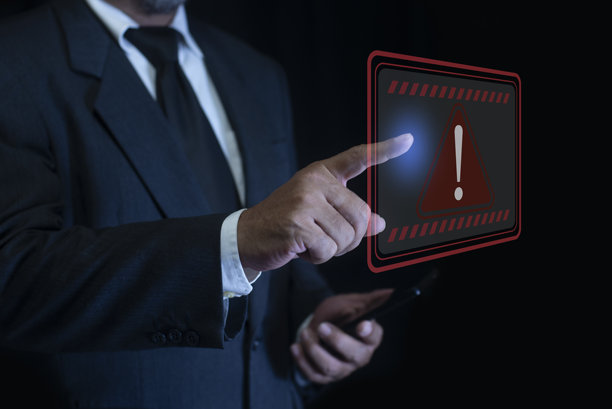 商人使用智能手机，屏幕显示网络网络攻击、系统被黑警告提示。手机上显示诈骗者警示和警告标识。图片下载