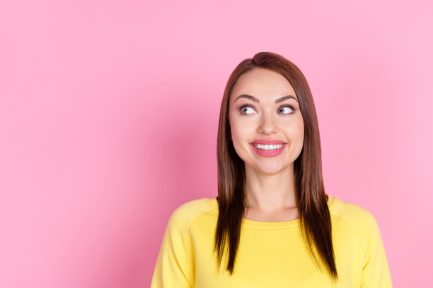 穿着黄色衣服的女孩的肖像照，她面带笑容，看起来很开心，背景是粉彩粉红色，留有空白空间。图片下载