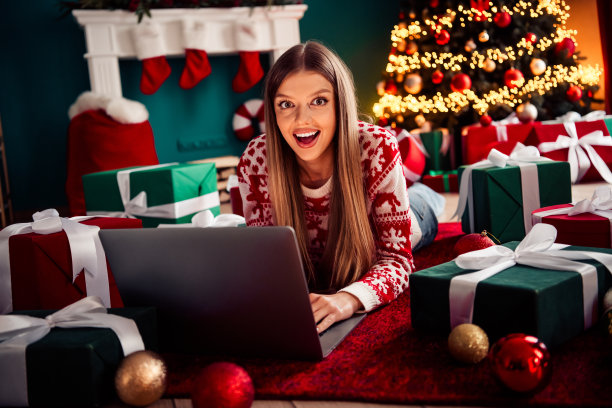 搞笑的节日购物女孩，在笔记本电脑旁，背景是圣诞树、礼物和温馨的家居场景，适合用作素材照片图片下载