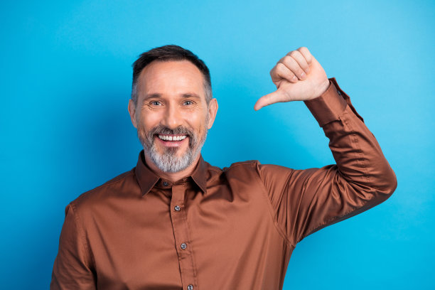 自信的成熟商人，身穿棕色衬衫，在蓝色背景前竖起大拇指，象征着企业成功和专业生活方式的素材照片图片下载