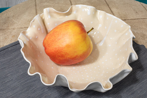 单个苹果放在带有褶边和波点图案的奶油色陶瓷碗里。水果展示，厨房装饰，静物。真实照片图片下载