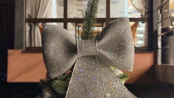 闪亮的银色蝴蝶结装饰的圣诞树顶部，置身于温馨的室内环境中——适合节日贺卡、冬季广告宣传、室内设计、博客、社交媒体、演示文稿和印刷品的照片。图片下载