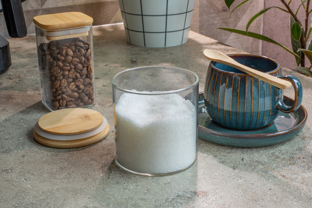 糖瘾概念。玻璃罐装糖和咖啡豆放在陶瓷马克杯旁，置于混凝土表面。咖啡冲泡、厨房收纳、饮品仪式。真实照片图片下载