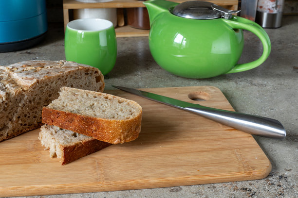 切片面包放在木质砧板上，旁边放着绿色的茶壶和马克杯。早餐布置，厨房场景，居家舒适。真实照片图片下载