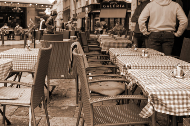 一张棕褐色调的街道咖啡馆图片，桌子已摆好但无人就座。图片下载