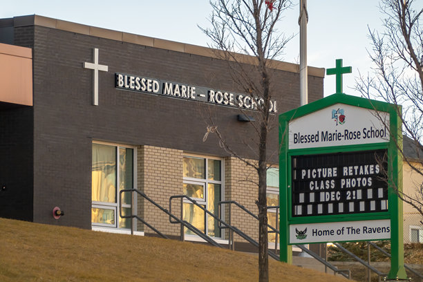 圣玛丽罗斯学校外观，展示了深色砖砌外墙、白色十字架和一个宣布补拍照片、班级照片和渡鸦吉祥物的绿色招牌。图片下载