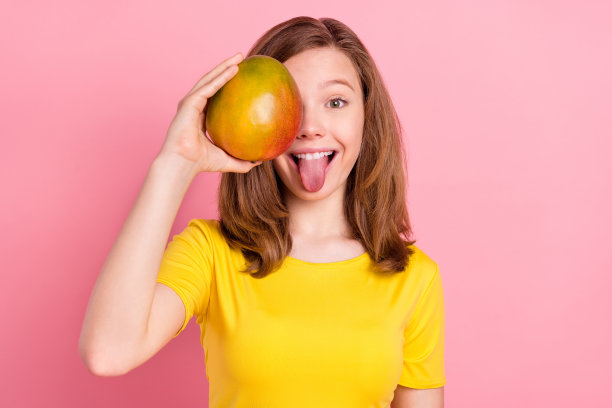 照片：粉色背景上，一个年轻女孩快乐地露出积极的笑容，遮住眼睛，吐着舌头做鬼脸。图片下载