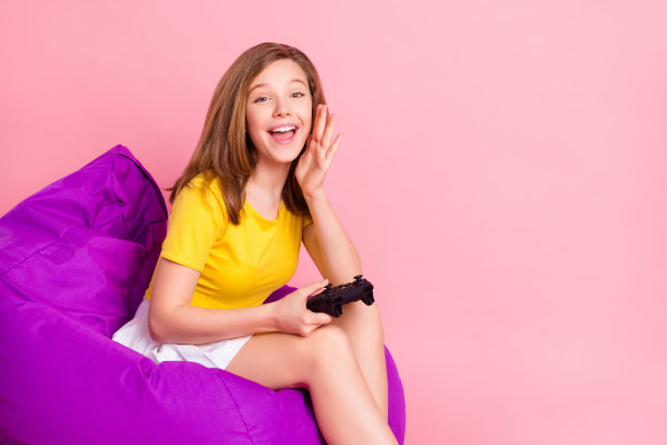 粉色背景下，穿着T恤和裙子的时髦棕发少女的个人资料照片，她戴着PlayStation头戴设备，孤立地坐着。图片下载