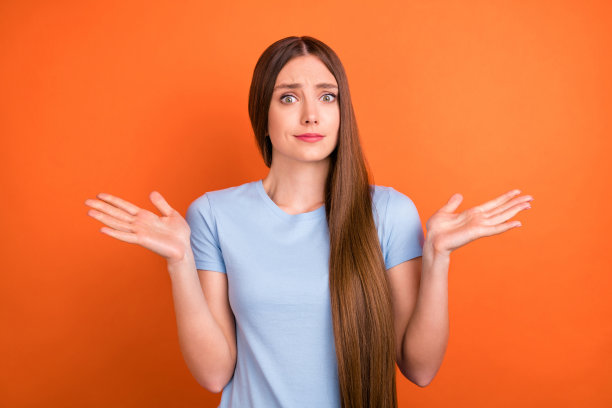 身穿蓝色T恤、棕色发型、印象深刻的千禧一代女士在鲜艳的橙色背景上耸肩的照片图片下载