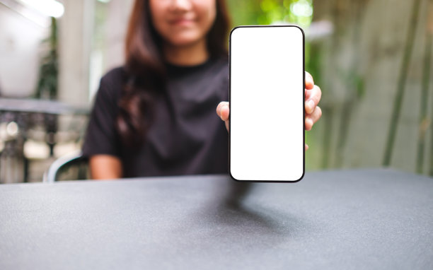 一名女子手持并展示带有空白白屏的手机的样机图图片下载