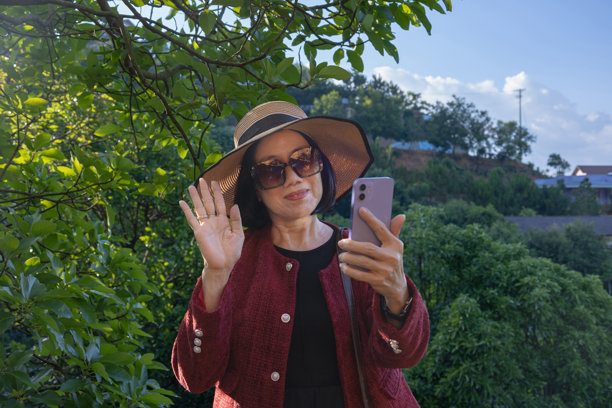 一位女士微笑着挥手，看着手机，可能是在打电话、发短信或进行视频通话。图库照片图片下载