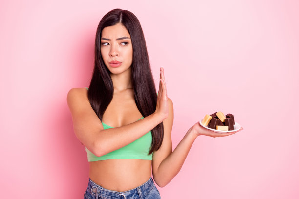 自信严肃的年轻女子，身穿绿色背心，在粉红色背景上拒绝巧克力甜食的特写照片图片下载