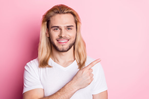 照片：英俊的年轻快乐男子手指指向粉色背景上的空白空间，宣传销售新闻图片下载