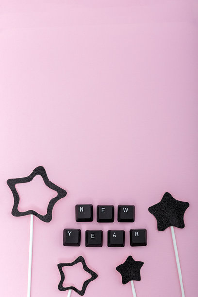 粉色背景上由键盘按键组成的“新年”字样，周围环绕着黑色的纸质星星。传达数字节日问候、在线庆祝和创意现代极简主义的概念。竖幅照片图片下载