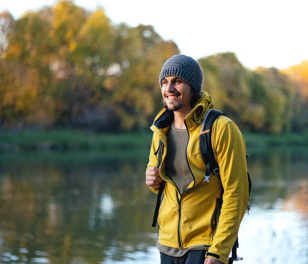 穿着黄色夹克和绒线帽的男人在湖边散步的素材照片图片下载