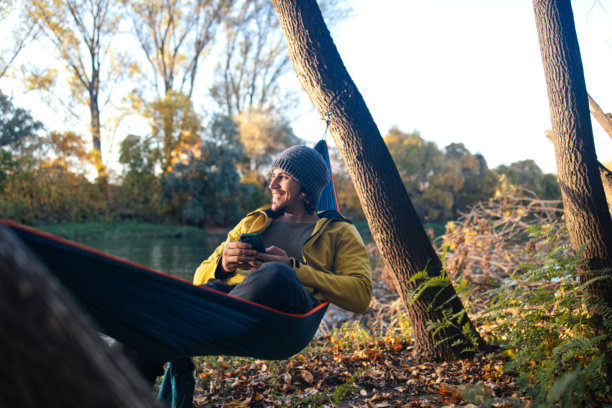 男人在河边吊床上休息，手中拿着手机的素材照片图片下载