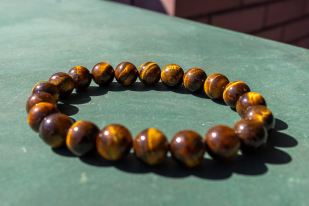 阳光下，虎眼石宝石珠手链在绿色背景上圆形排列的特写照片。图片下载
