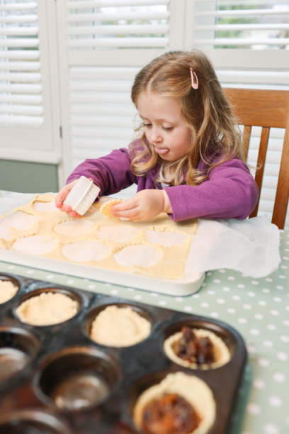 五岁的小女孩在厨房餐桌旁学习使用饼干模具切割酥皮派的形状，制作节日圣诞节肉馅饼。图片下载
