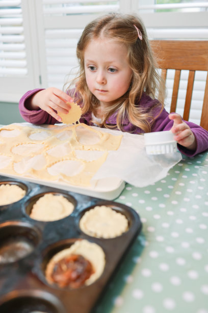 五岁的女孩在厨房餐桌上学习使用饼干模具切割起酥皮，制作节日圣诞肉馅饼图片下载