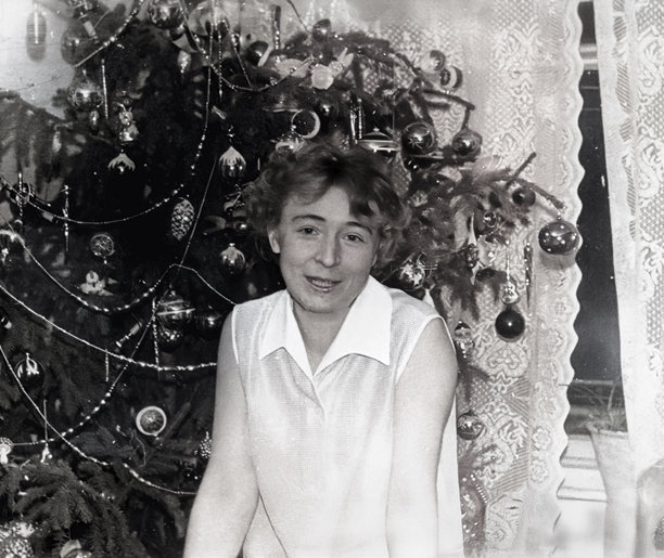 一位美丽的年轻女子在圣诞树旁微笑的复古肖像。摄于1965年的老照片。图片下载