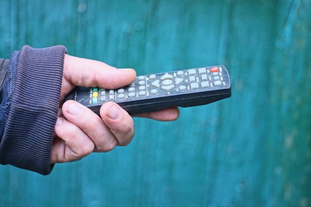 一只手拿着一个旧的黑色塑料电视遥控器图片下载