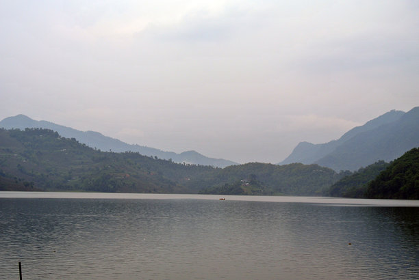 这张照片展示了一个宁静的湖泊，周围环绕着绿色的山丘和远处的山脉。图片下载
