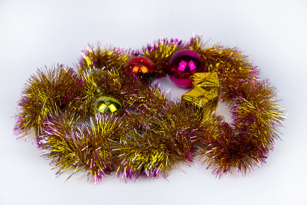 闪亮的金色彩带缠绕着粉色点缀，围绕着白色背景上的圣诞彩球和金色小礼品盒。这些节日装饰营造出明亮、欢乐的场景。柔焦新年照片。图片下载