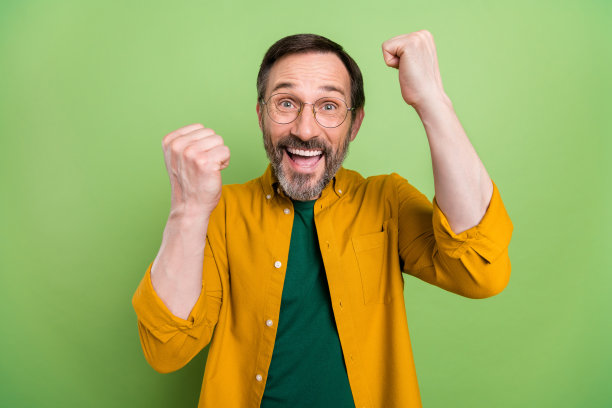 照片：一位成熟的男人，脸上带着快乐积极的微笑，庆祝胜利，好运，成功，握紧拳头，双手，孤立在绿色背景上图片下载