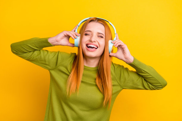 红发女子戴着耳机听音乐大笑，背景是鲜艳的黄色，孤立的照片肖像图片下载