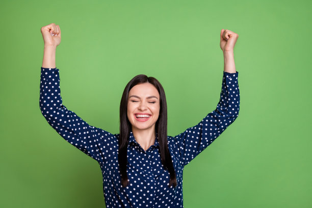 照片：惊讶的棕色头发女CEO双手举起，身穿蓝色衬衫，孤立在绿色背景上图片下载