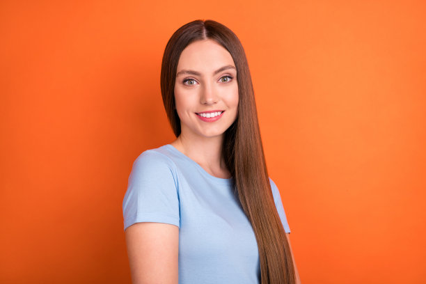 身穿蓝色T恤、拥有可爱长发的年轻女子，在鲜艳的橙色背景中拍摄的照片图片下载