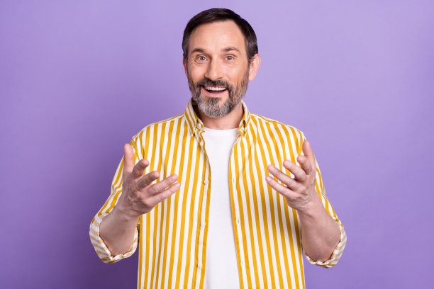 照片：一位穿着黄色衬衫、面带微笑、表情惊讶的老先生，正对着镜头说话，背景为紫色。图片下载