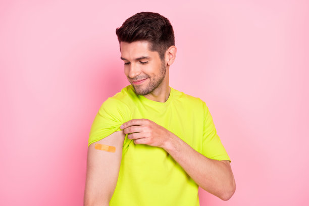 照片：乐观的棕色发型年轻男子，穿着绿色T恤，接种疫苗，背景为粉色图片下载