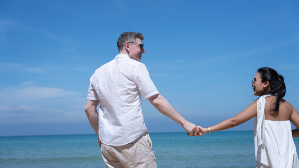 浪漫情侣在海滩上享受阳光明媚的一天，身着白色服装在海边漫步。非常适合旅行、蜜月、浪漫、暑假和生活方式概念的图片。图片下载