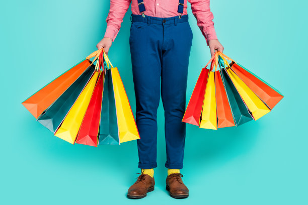 黑五促销期间，年轻男子拎着购物袋的特写照片，背景为蓝绿色图片下载