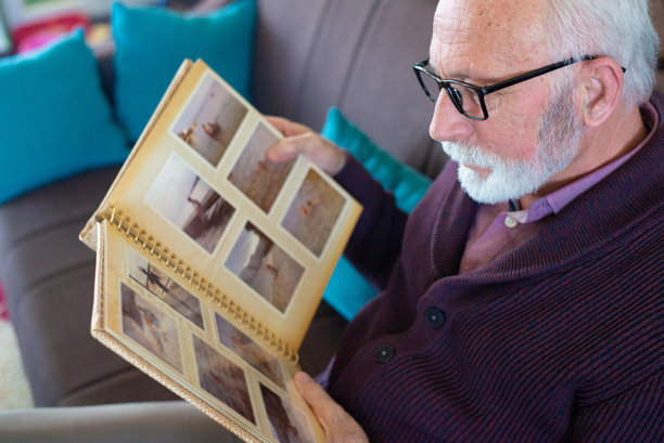 冬天，一位年长男子在家中坐着，翻看相册里的照片。图片下载