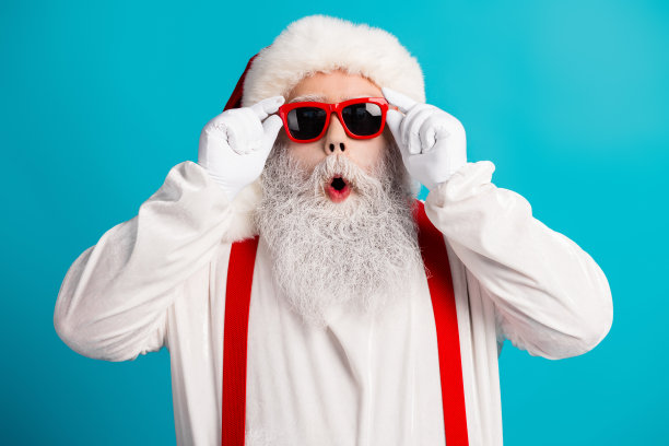 圣诞老人穿着红色吊带和眼镜，在明亮的蓝色背景前摆出有趣的节日姿势，适用于假日季素材图图片下载