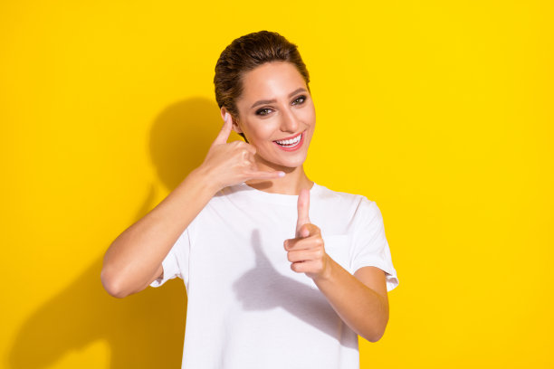 照片：一个年轻女孩露出快乐积极的笑容，做出打电话、交谈、选择、挑选的手势，手指指向你，背景为孤立的黄色图片下载