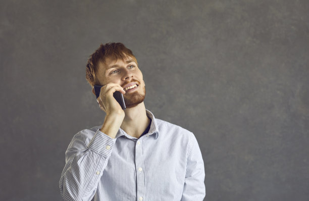 面带微笑的男人，在灰色背景前站着打电话图片下载